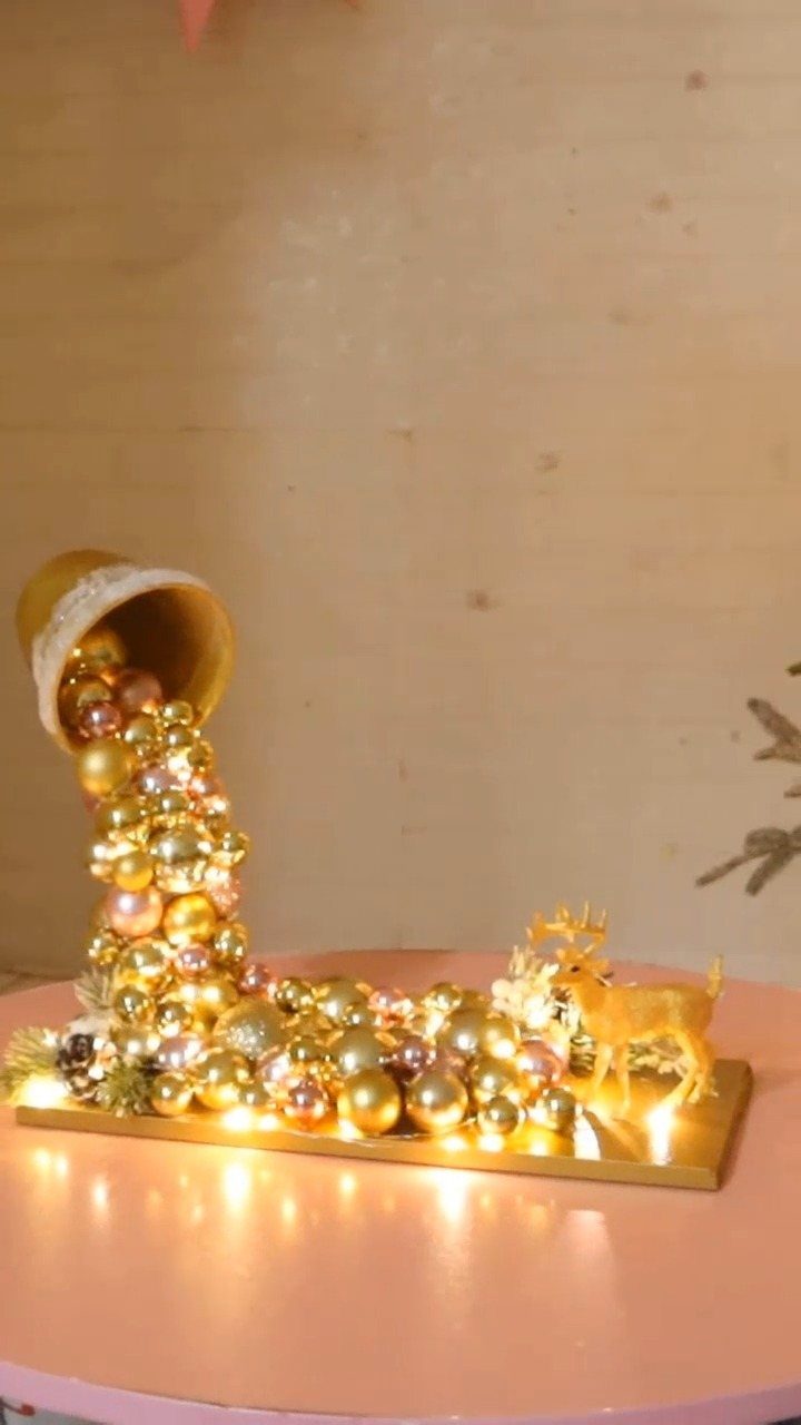 Gold bucket spilling shimmering Christmas ornaments and lights with a small golden reindeer