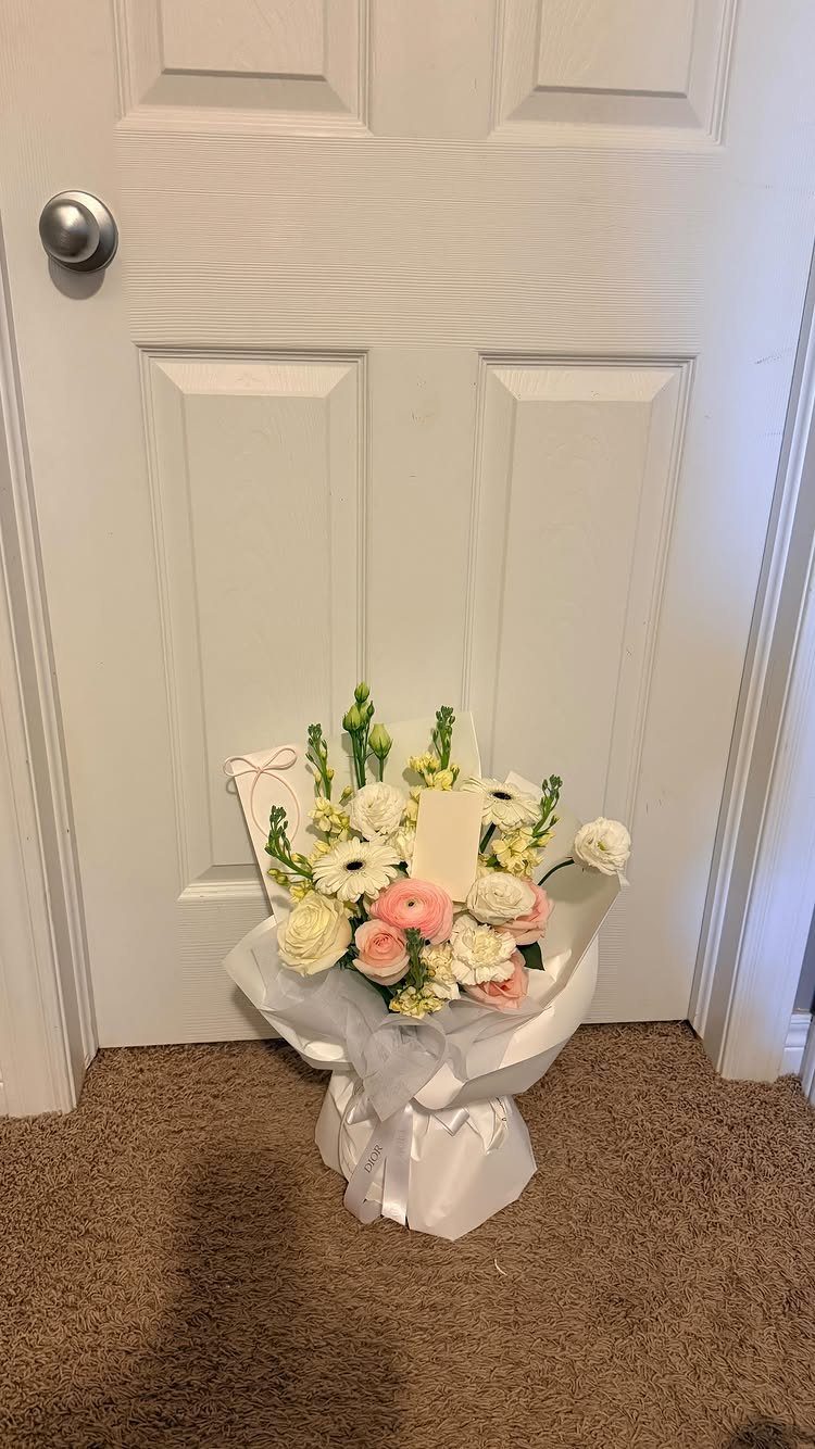 Bouquet of white and pink flowers wrapped in white paper on a carpeted floor.