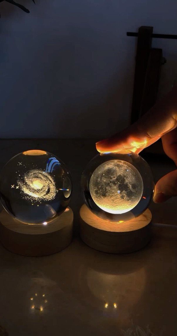 Two glowing glass spheres depicting a galaxy and the moon on wooden bases.