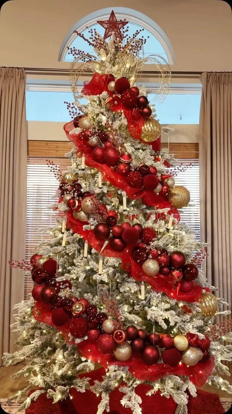 Flocked white Christmas tree decorated with red and gold ornaments and red ribbons.