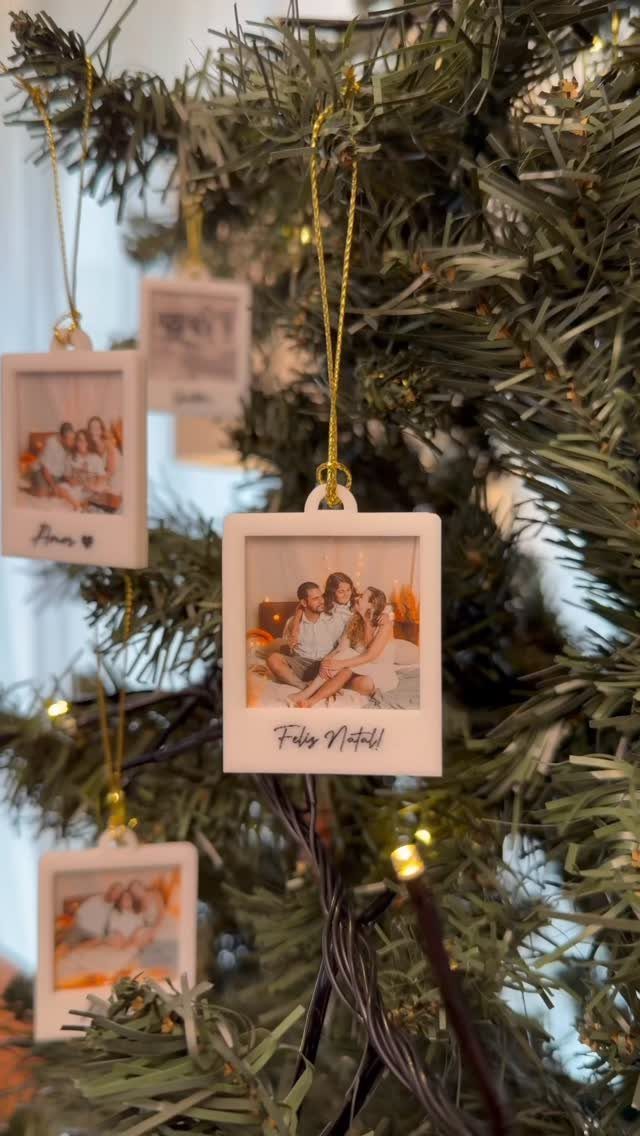 White framed photo ornaments hanging on a green Christmas tree with warm lights.