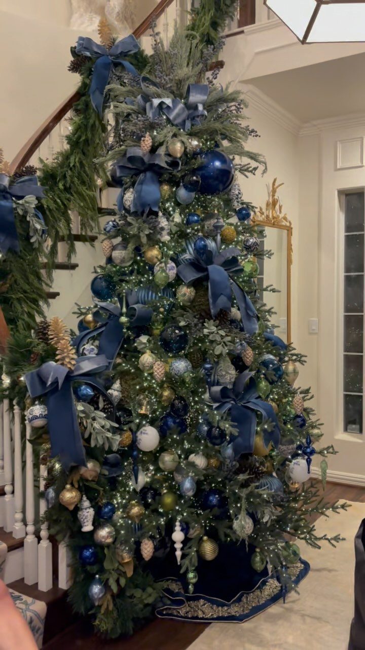 Decorated Christmas tree with navy blue ribbons and gold ornaments in a home entryway
