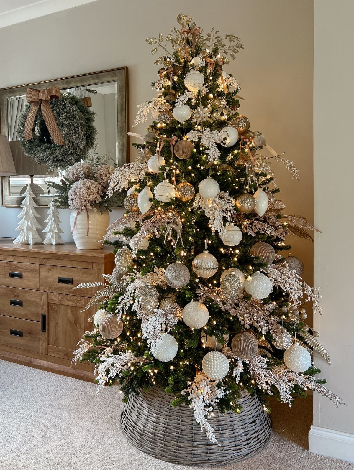 Decorated Christmas tree with neutral white and gold ornaments in a wicker basket.