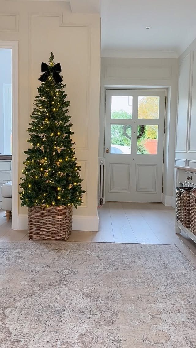Green Christmas tree with warm lights and a black bow in a wicker basket.