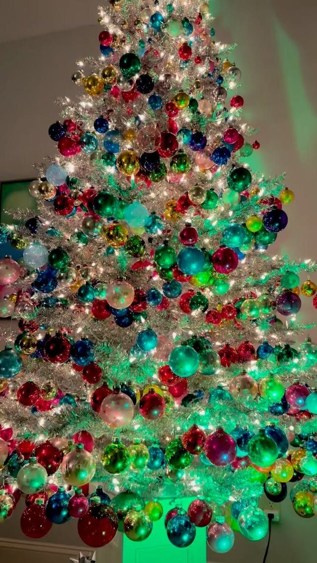 Christmas tree covered in silver tinsel and colorful glossy ornaments with glowing lights.