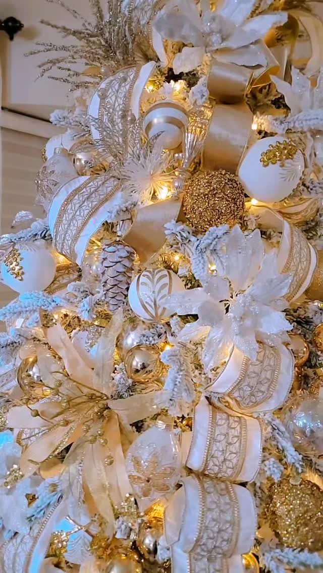 Elegant Christmas tree decorated with gold and white ornaments, ribbons, and white flowers.
