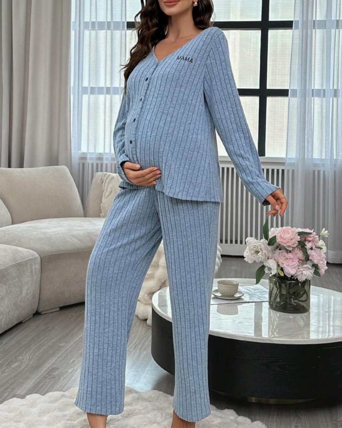 Pregnant woman wearing light blue ribbed pajamas with MAMA text in a living room