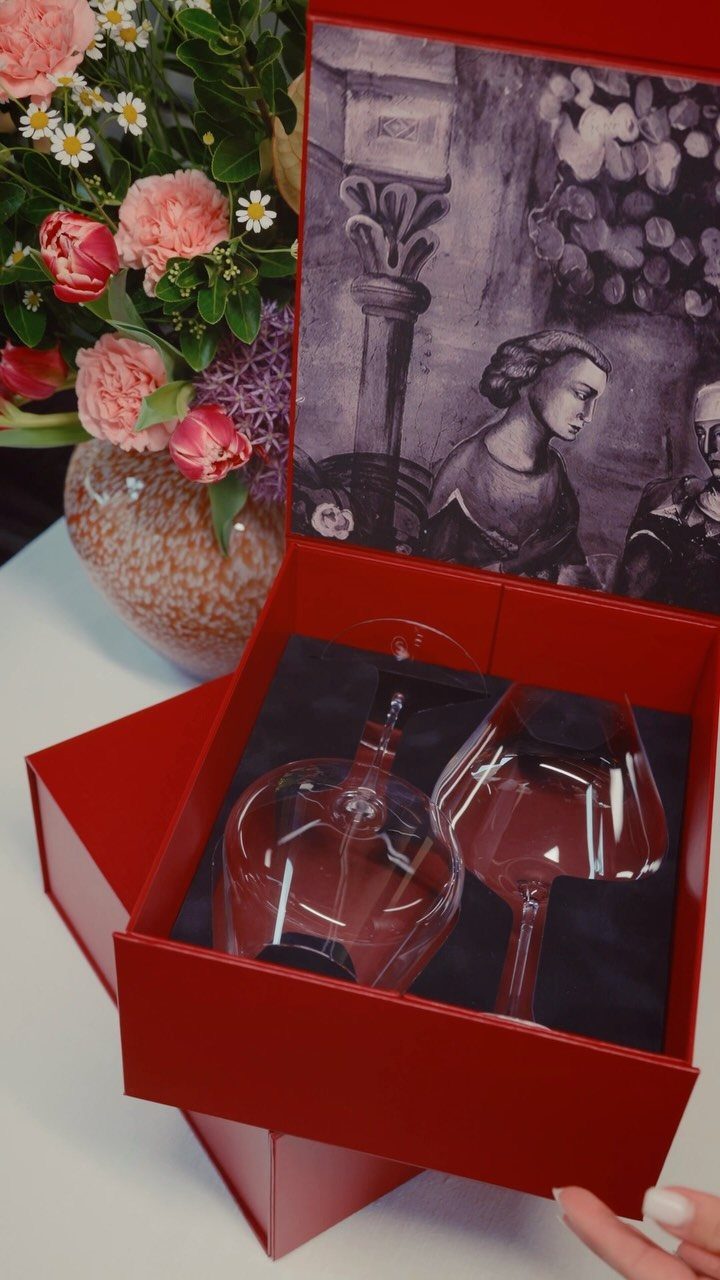 Glass decanter and wine glass in a red gift box next to flowers