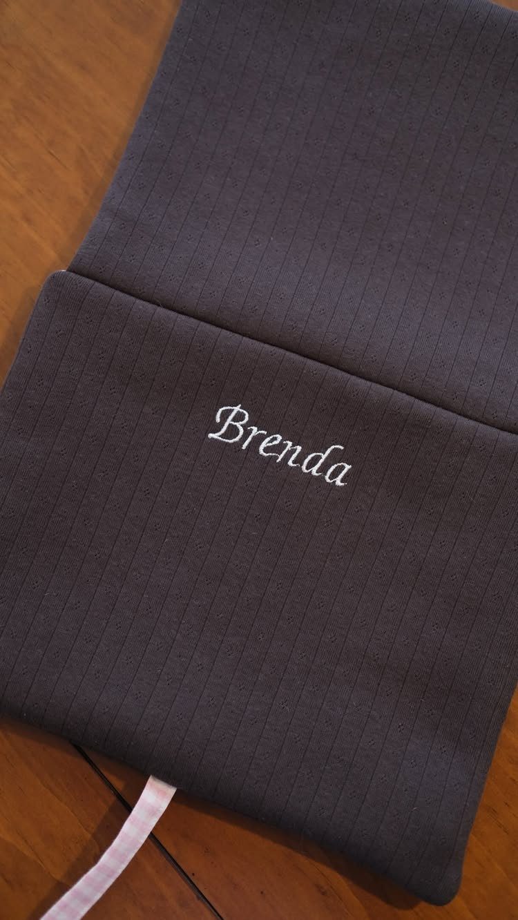 Dark grey ribbed fabric cover with the name Brenda embroidered in white script.