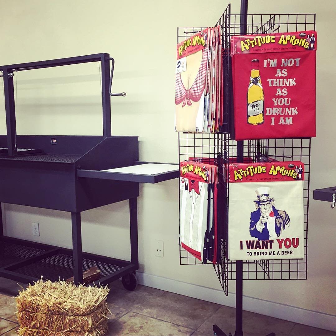 Novelty BBQ aprons with funny slogans displayed on a black metal rack.