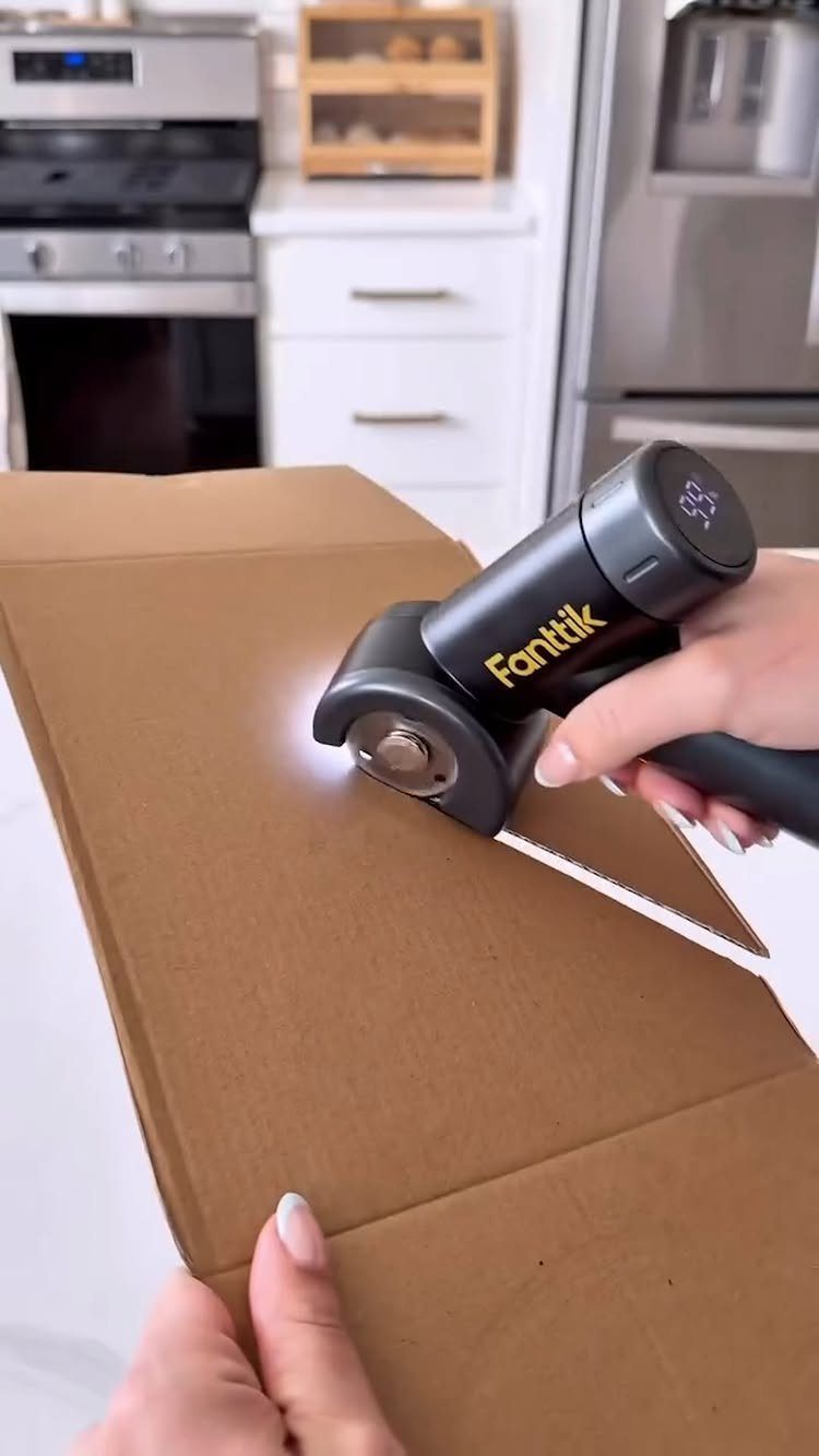 Electric box cutter slicing through a brown cardboard box in a kitchen