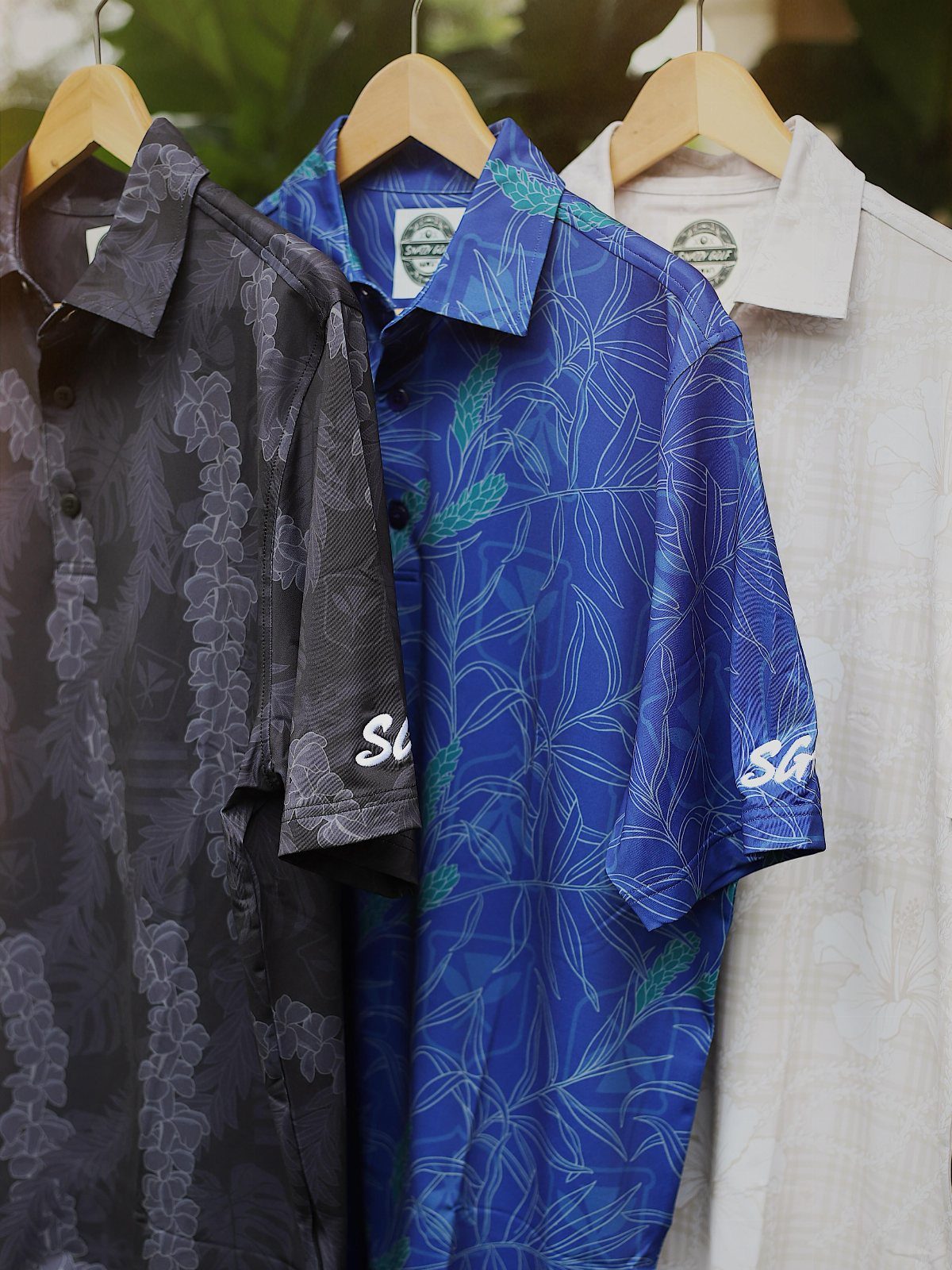 Three patterned button-down shirts in black, blue, and white hanging on wooden hangers.