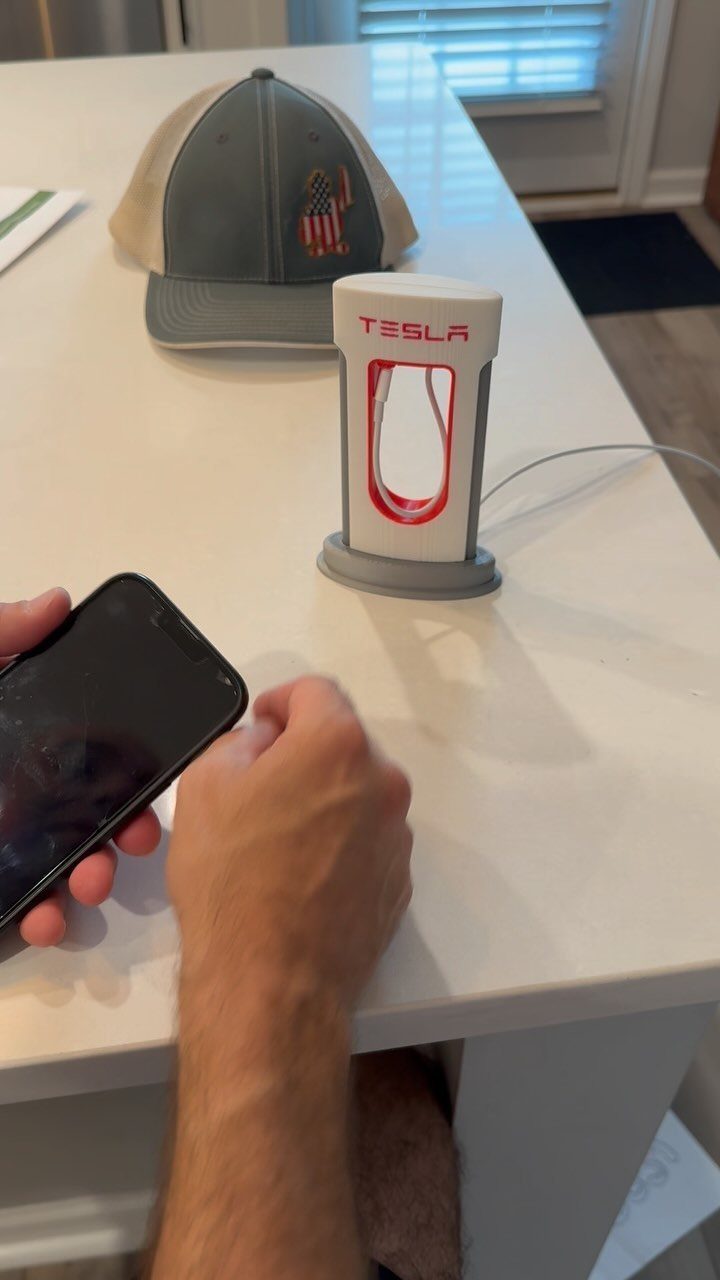 Tesla branded novelty lamp and baseball cap on a white table next to smartphone