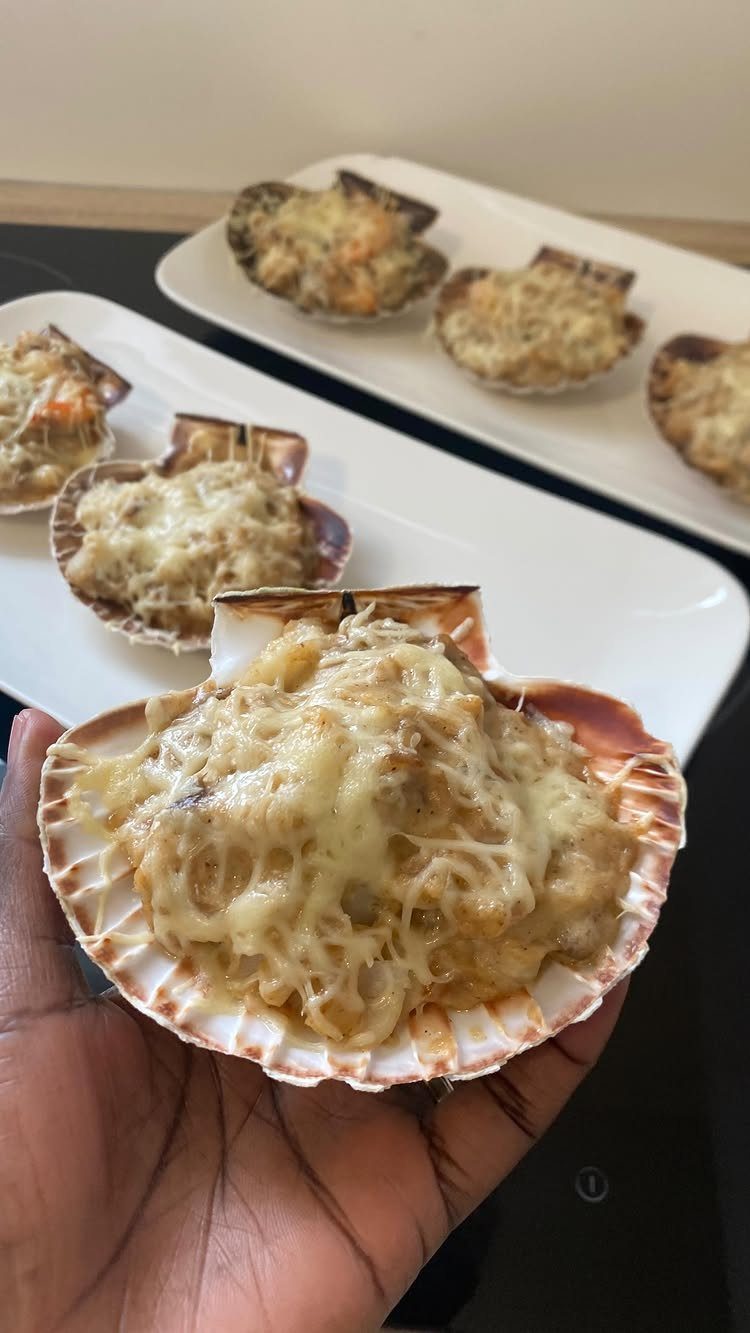Baked cheesy seafood appetizers served in natural scallop shells on white platters.