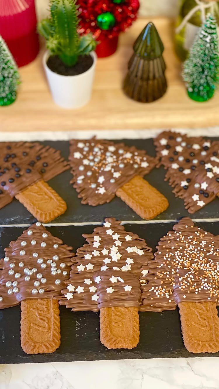 Chocolate covered tree-shaped cookies with white and silver sprinkles on a black platter
