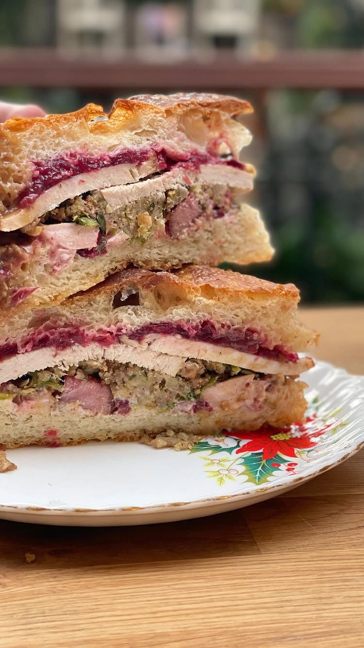 Layered turkey sandwich with cranberry sauce and stuffing on a festive plate.