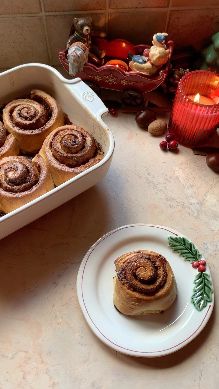 Cinnamon rolls in a baking dish and on a plate with holiday decorations.