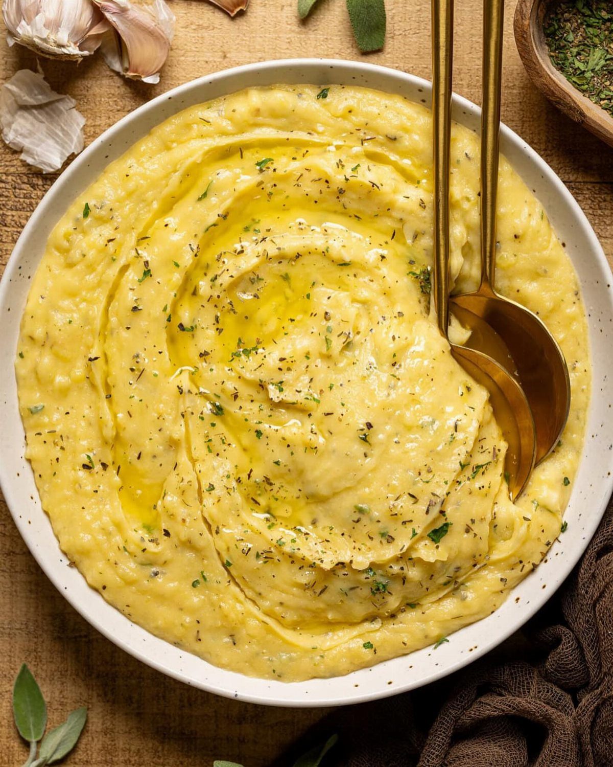 Creamy mashed potatoes in a white bowl topped with melted butter and herbs.
