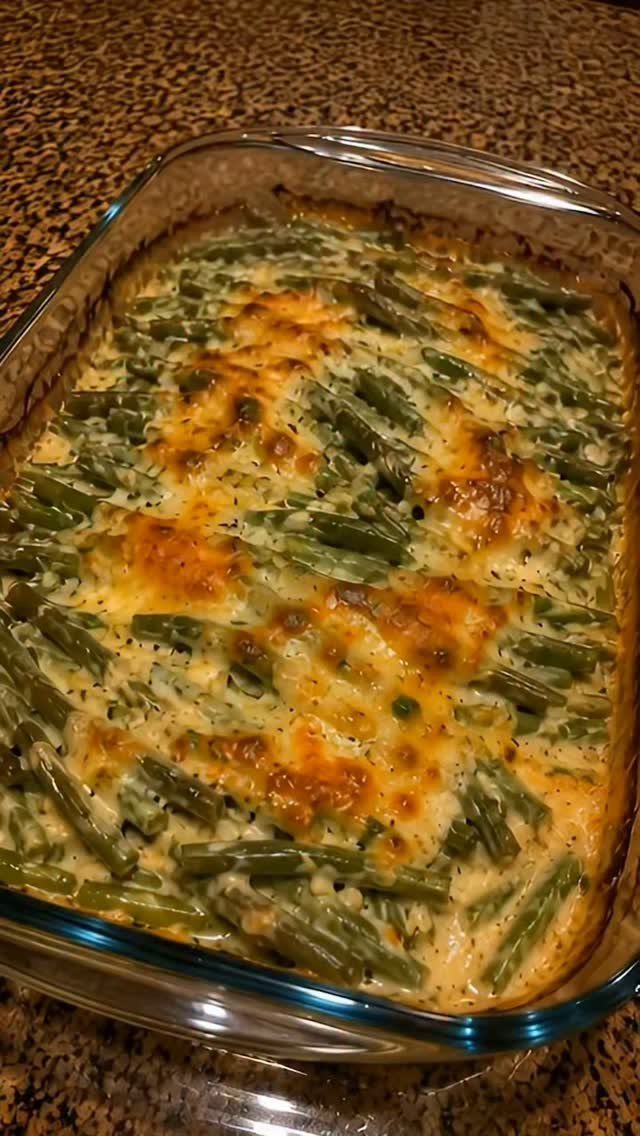 Green bean casserole with melted browned cheese in a glass baking dish.
