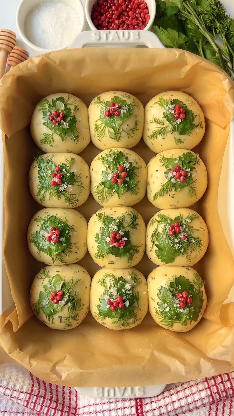 Twelve dinner rolls decorated with dill and red berries in a baking dish