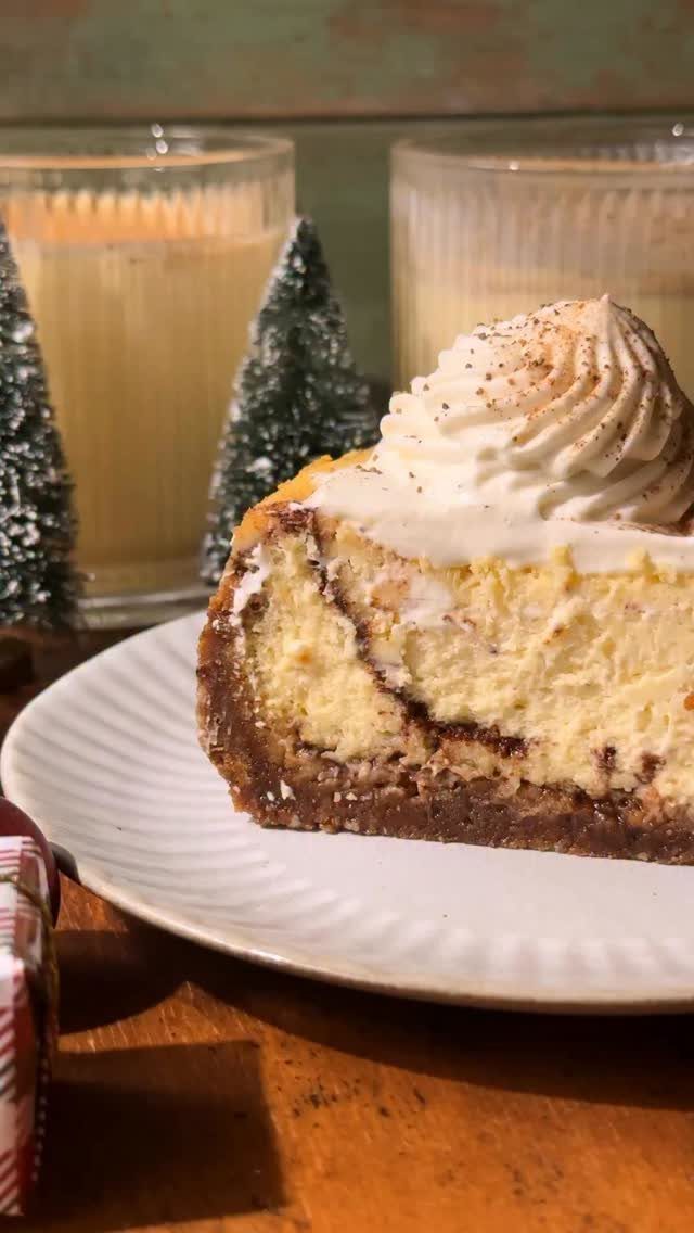 Cheesecake slice with whipped cream topping served with glasses of eggnog and mini trees.
