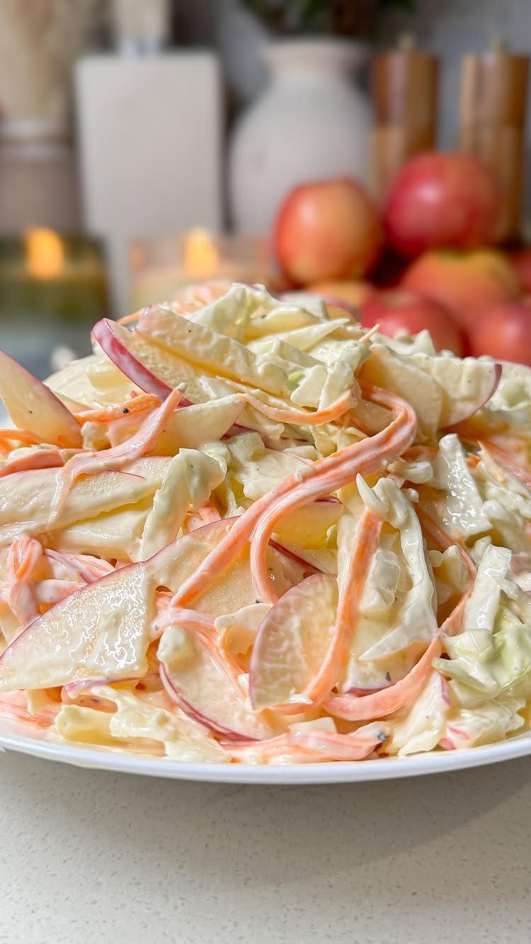 Creamy apple salad with sliced red apples and shredded cabbage on a white plate.