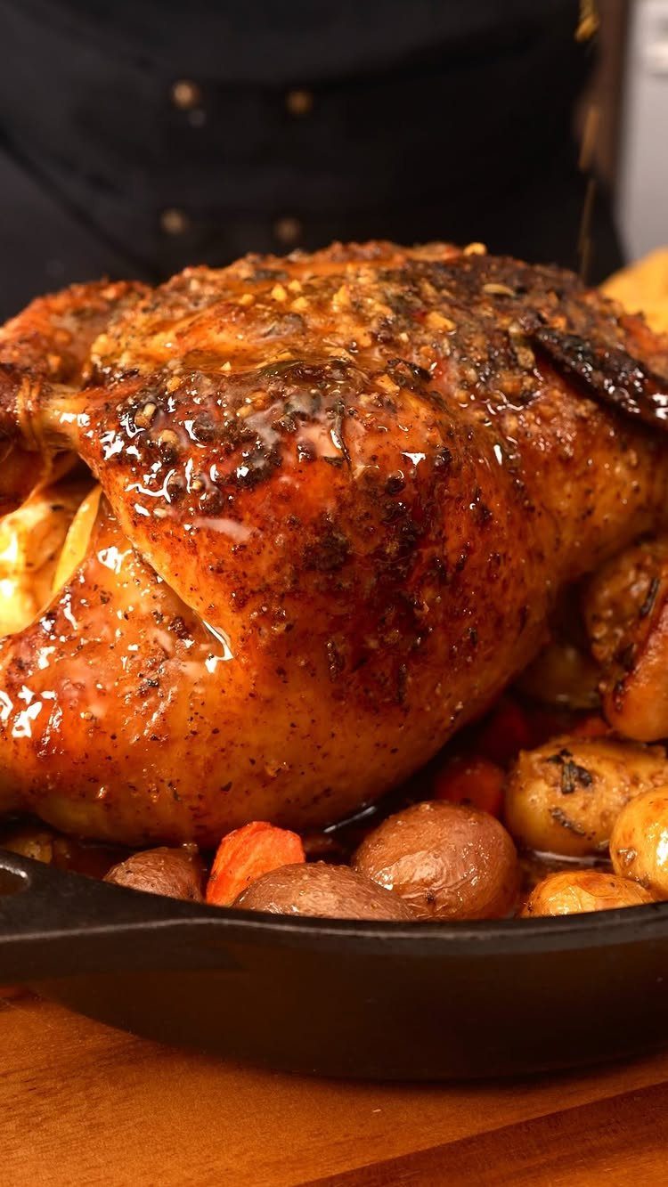 Roasted whole chicken with herbs and vegetables in a black cast-iron skillet