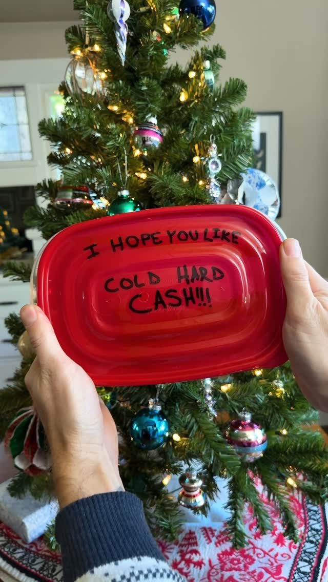 Red baking dish with funny cash message held before a decorated Christmas tree