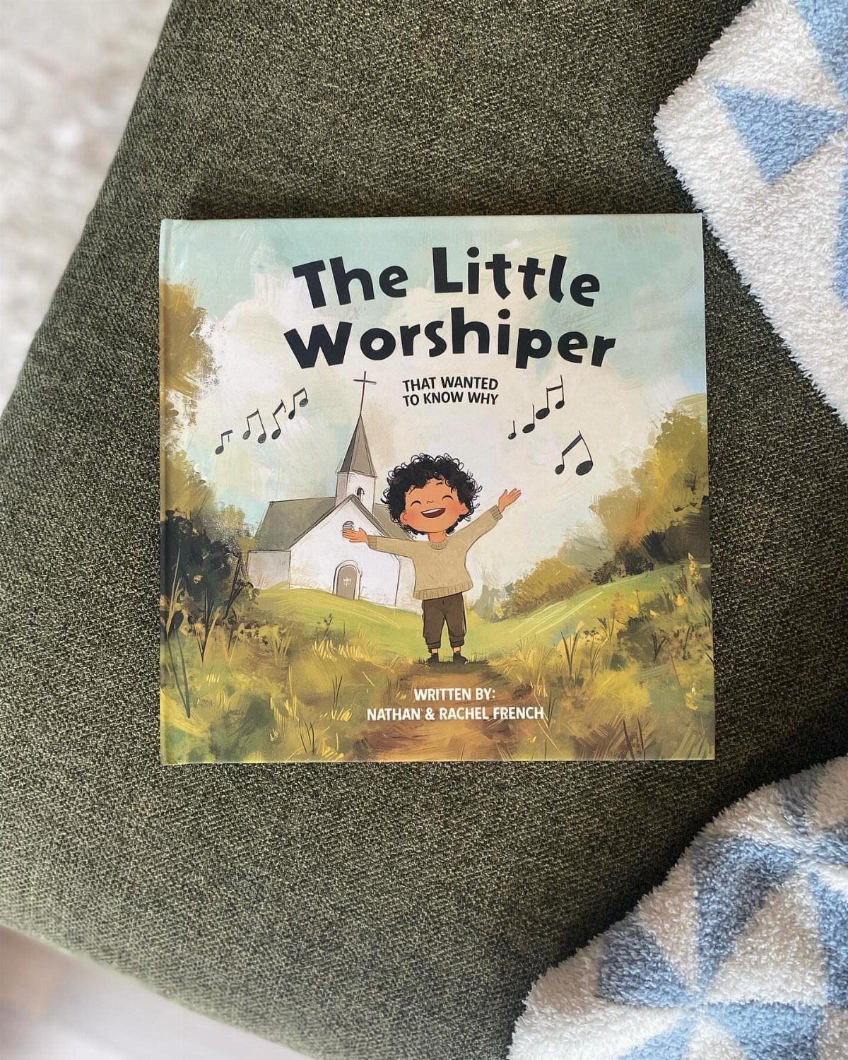 The Little Worshiper children's book resting on a green textured fabric surface