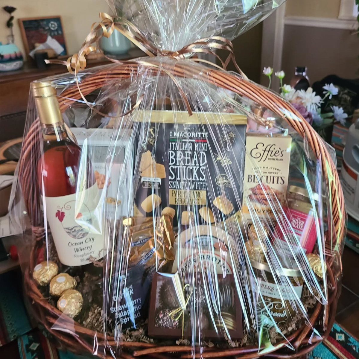 Wicker gift basket containing a bottle of rosé wine and gourmet snacks.