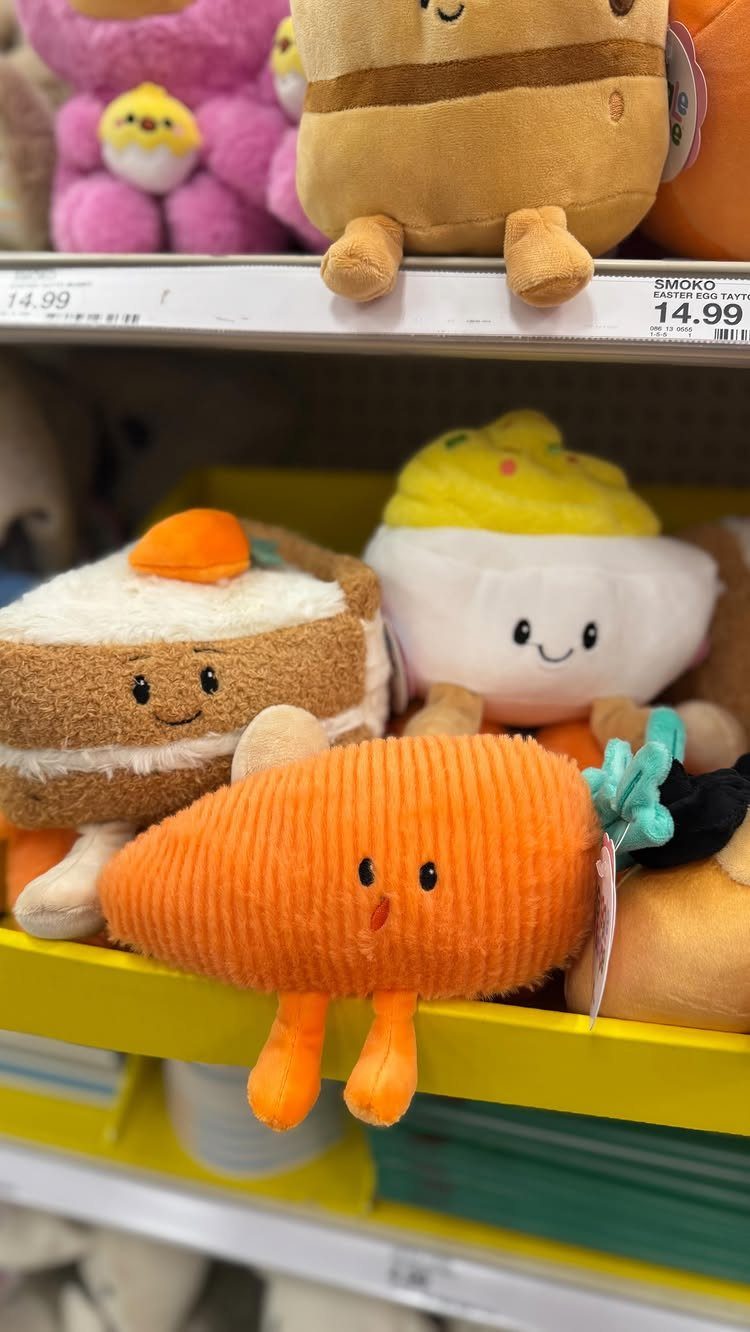 Plush carrot and dessert toys with smiling faces on a retail store shelf.