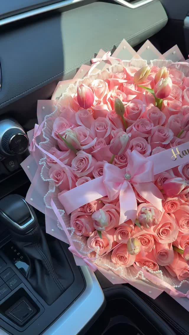 Large bouquet of pink roses and tulips with a bow in a car