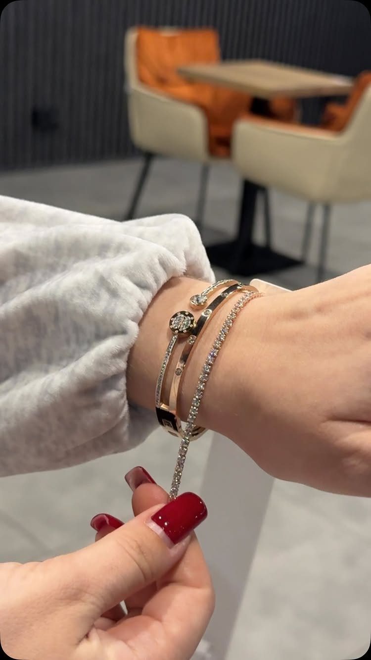 Gold and silver crystal bracelets on a wrist being adjusted by red nails.
