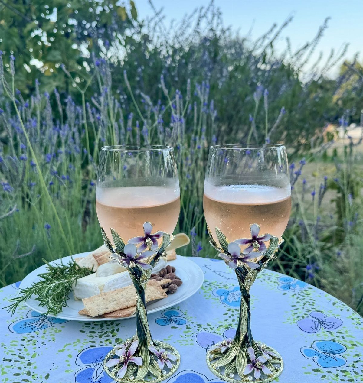 Two ornate wine glasses with floral stems filled with rosé on a floral table.