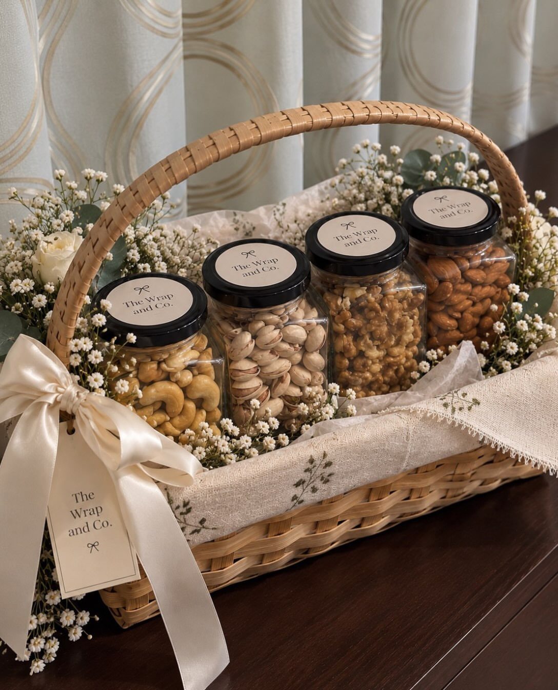 Woven gift basket with four jars of nuts, white flowers, and a satin bow.