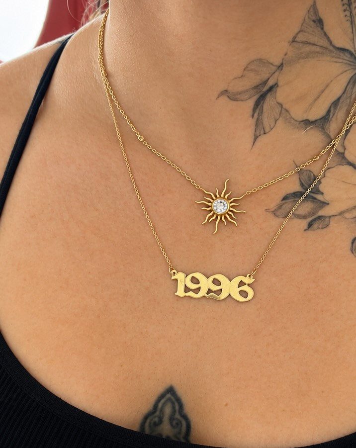 Two layered gold necklaces with a sun pendant and 1996 year pendant.