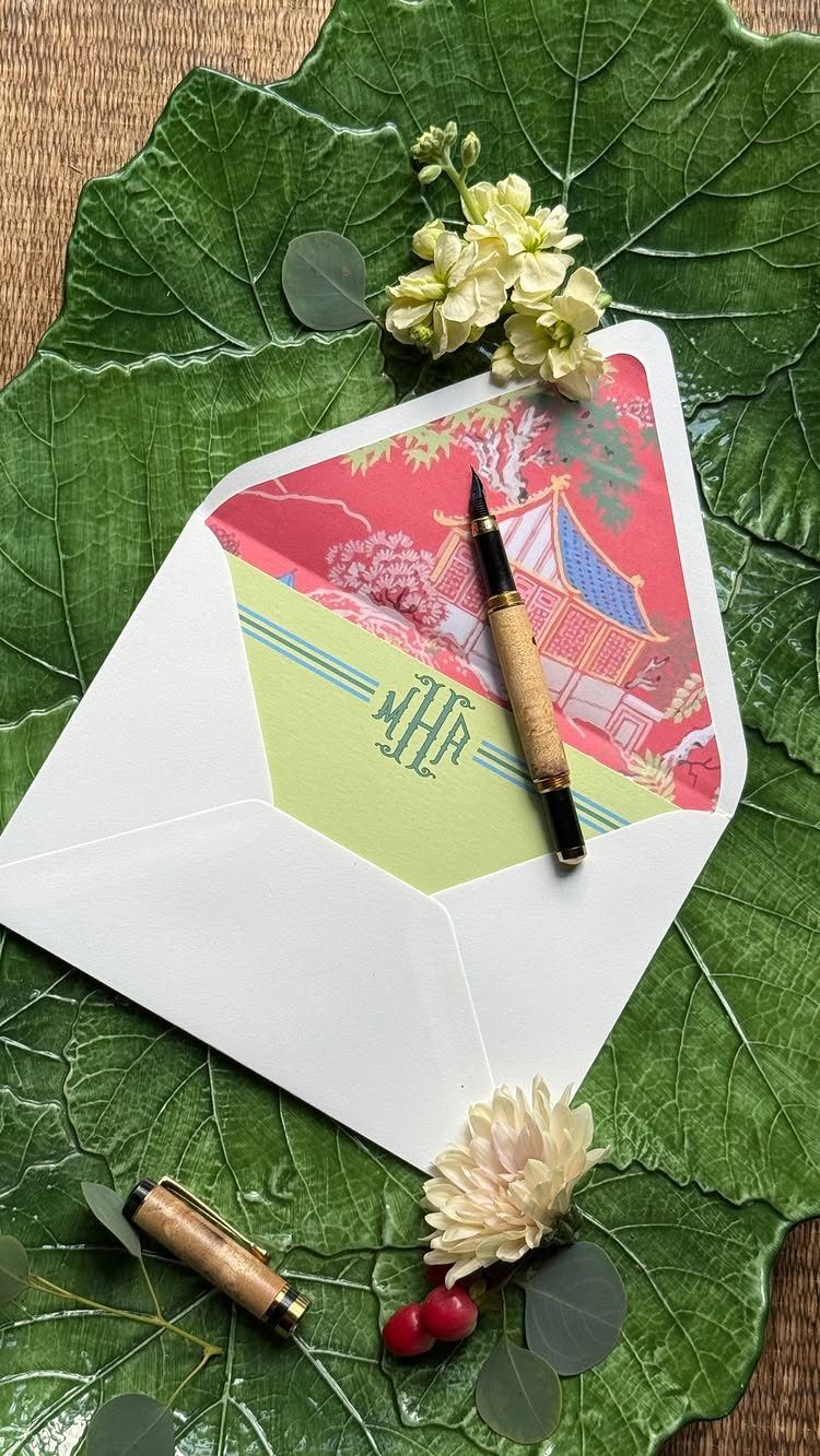 Open white envelope with monogrammed lining and fountain pen on a green leaf