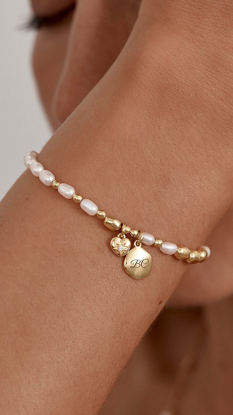 Gold and pearl bracelet with engraved initials and heart charm on a wrist
