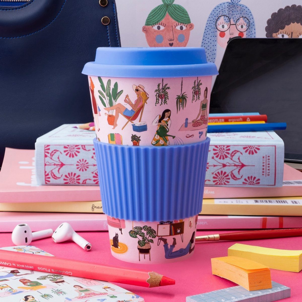 Illustrated travel mug with blue lid and sleeve on a pink desk setup.
