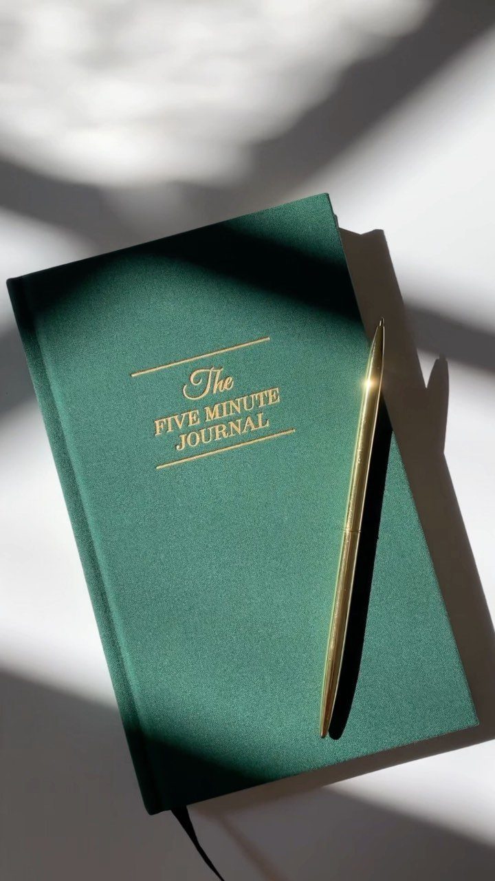 Green Five Minute Journal with a gold pen on a white surface.