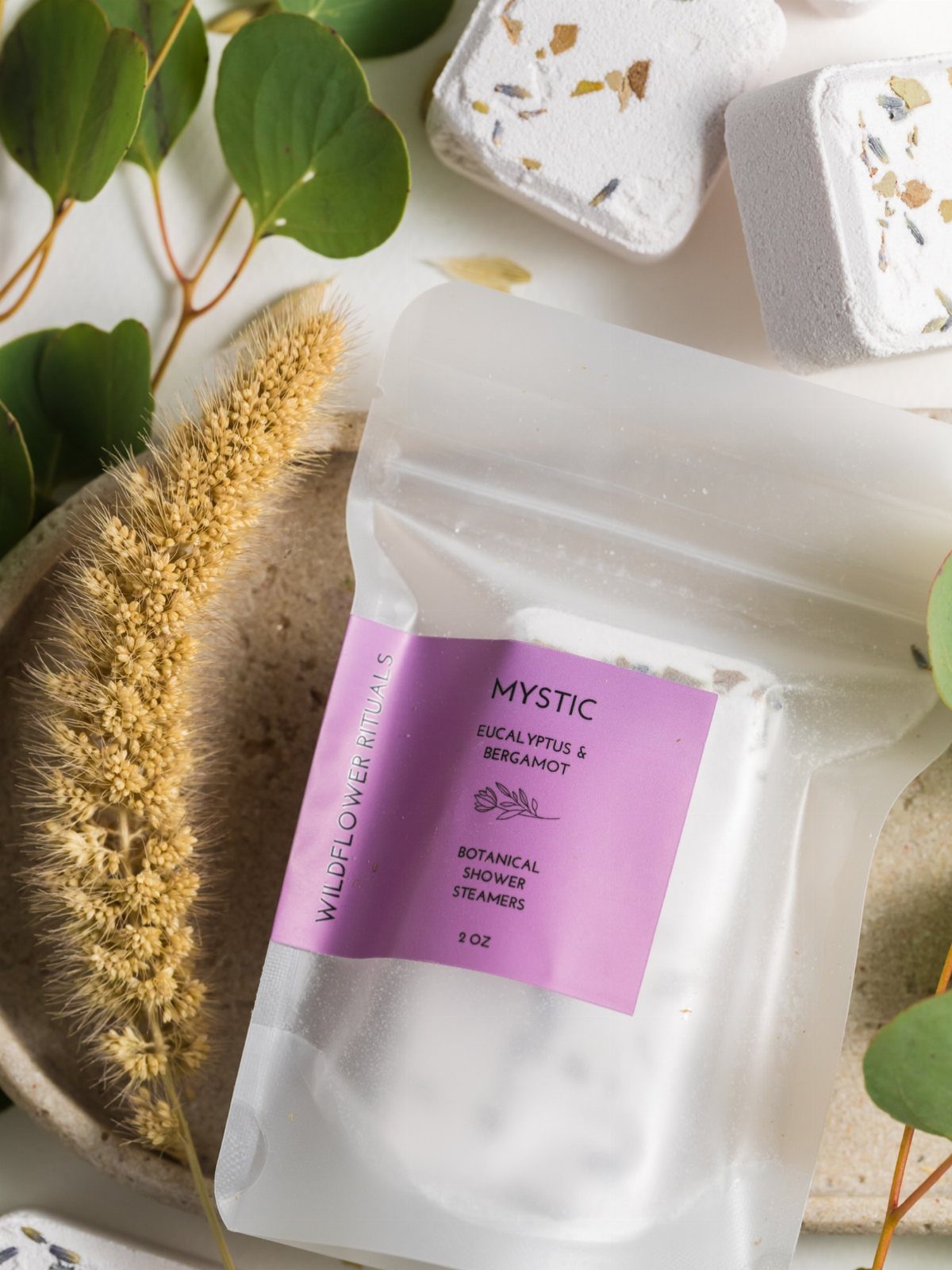 Botanical shower steamers in a frosted pouch with white tablets and eucalyptus leaves.