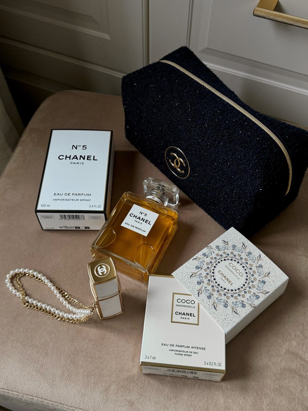 Chanel N°5 perfume bottle and box next to a black glittery makeup bag.