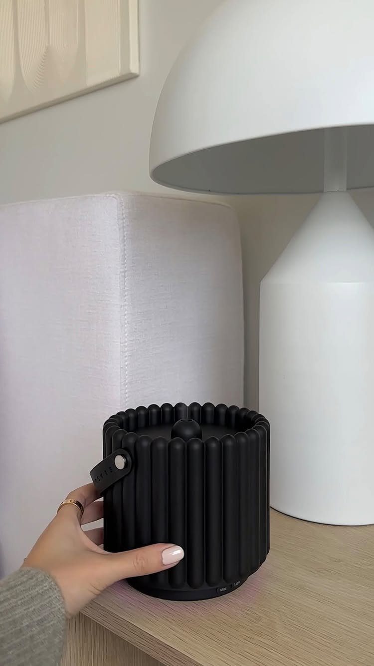Black ribbed portable speaker held by a hand on a wooden table