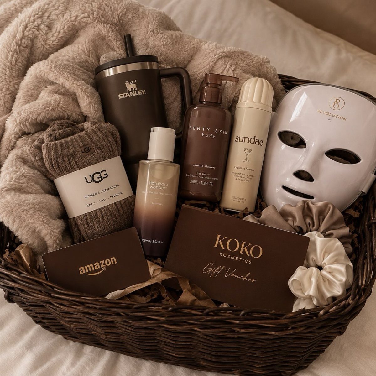Wicker gift basket filled with skincare products, a tumbler, socks, and a face mask.