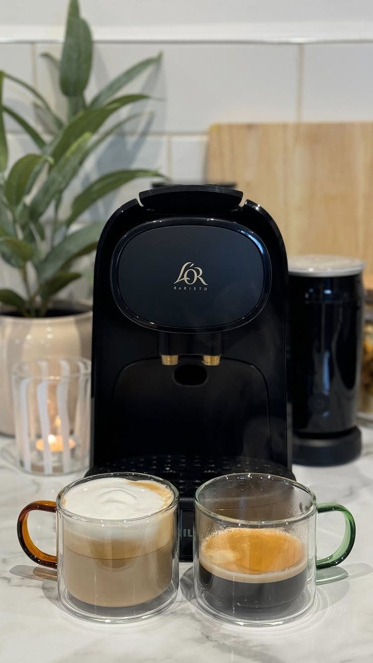 Black espresso machine with two glass cups of coffee on a marble counter.