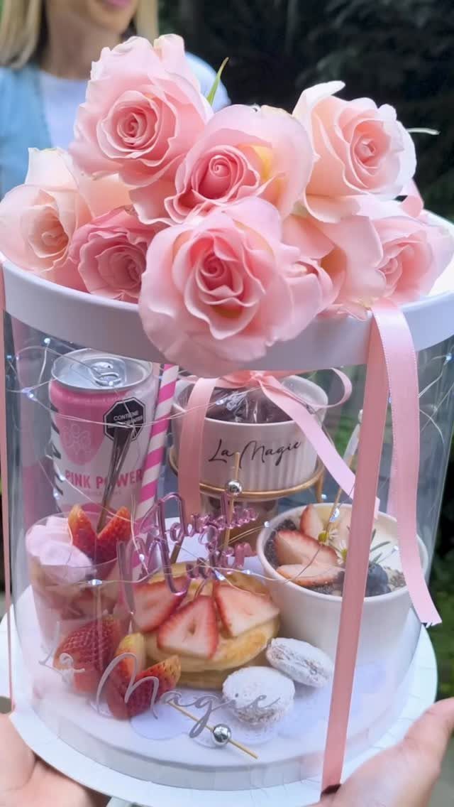 Gift box with pink roses, fresh strawberries, macarons, and a small cake.