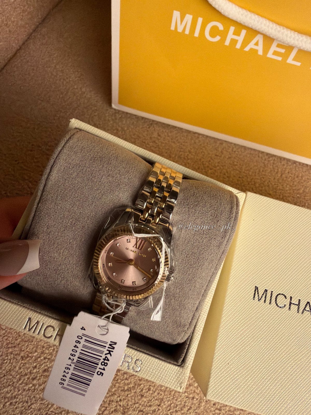 Gold Michael Kors wristwatch in a white gift box with a yellow shopping bag.