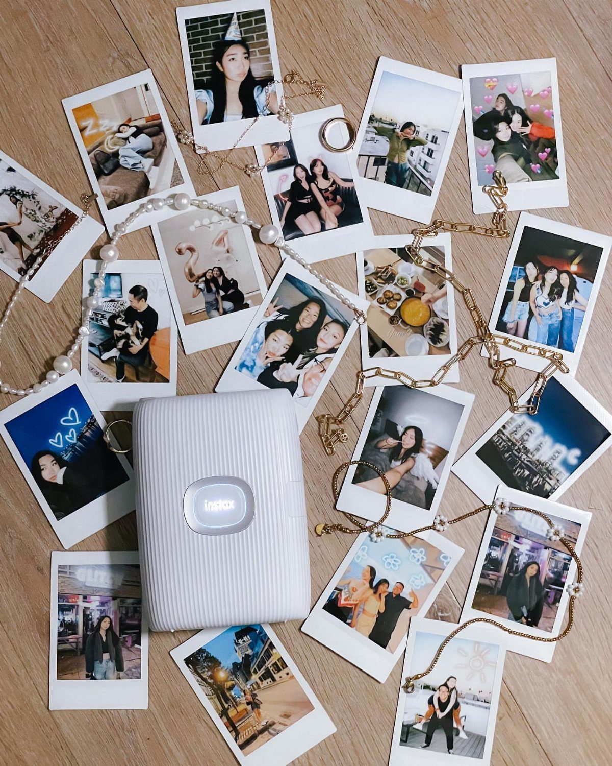 White instant camera case surrounded by scattered instant photos on a wooden surface.