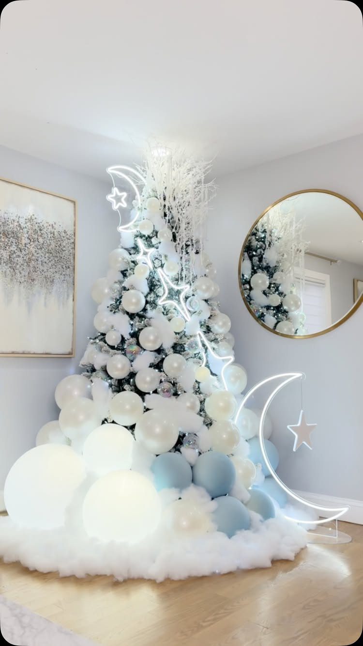 White flocked Christmas tree with blue ornaments and glowing neon moon and star decorations.