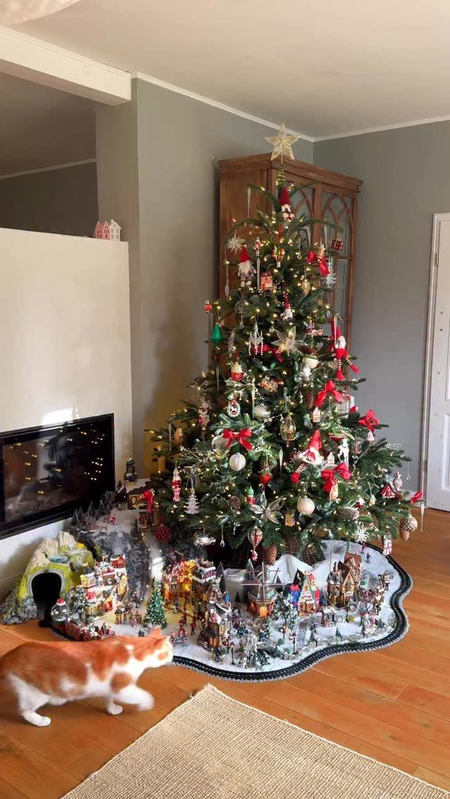 Decorated Christmas tree with a miniature snowy village display and a walking cat.